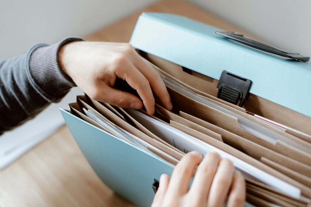 pexels-photo-4792285-4792285 Close-up of hands organizing papers in a blue folder, ideal for business and office concepts.